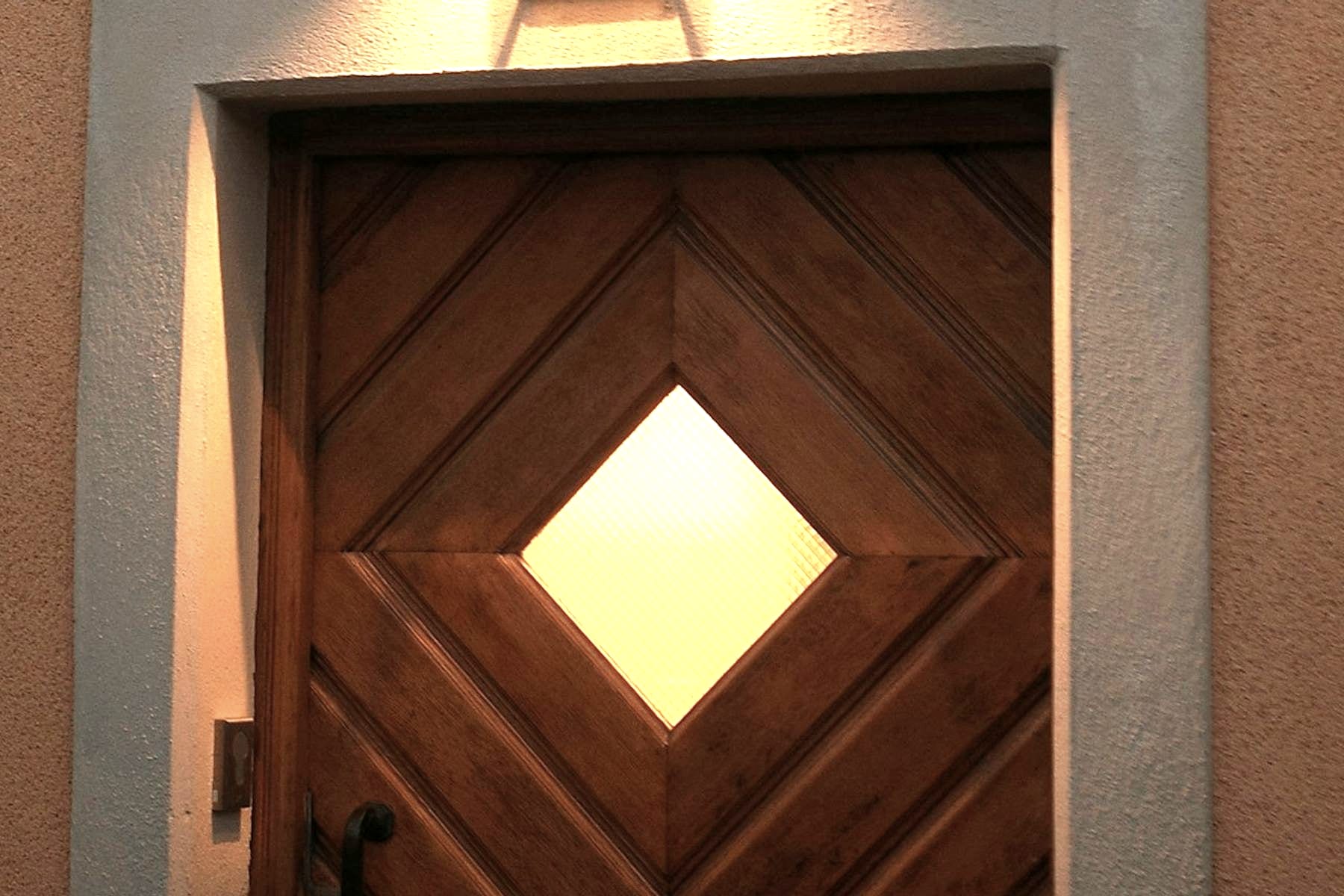 The street door at dusk, lit from above, a diamond of ribbed glass set in the panelling.