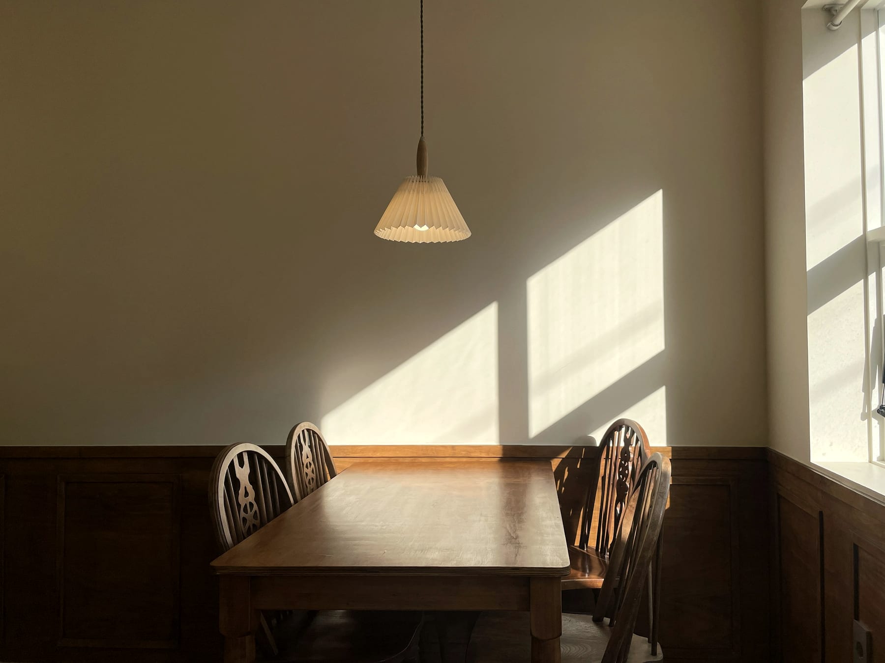 A plain wooden table and chairs in window light.